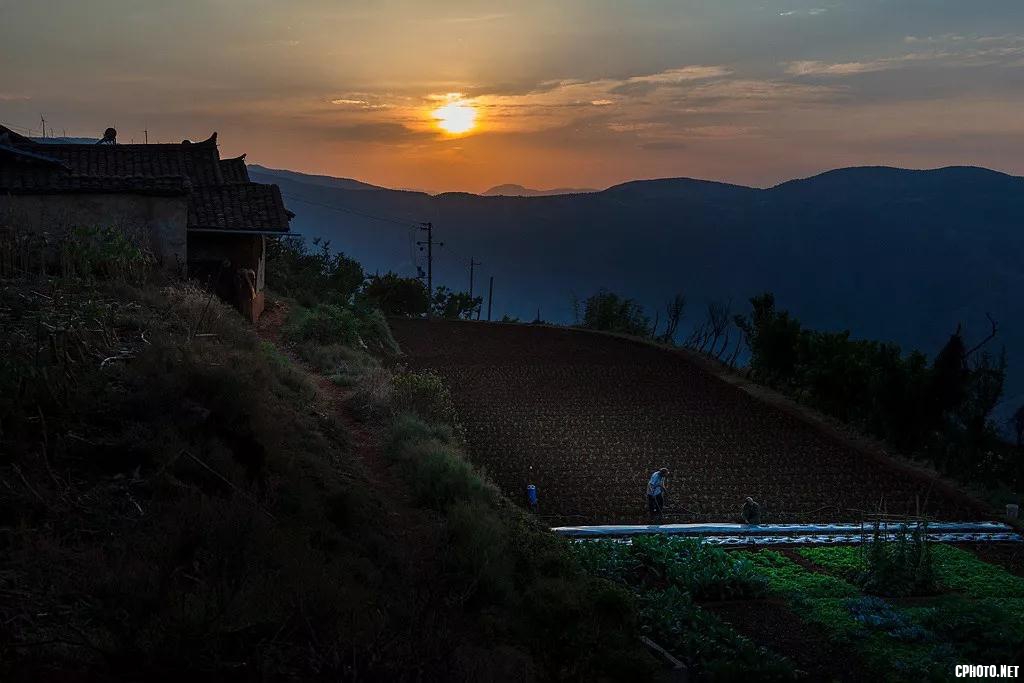 黄昏时分仍在地里劳作的人们。太阳落山的地方是云南的龙潭山脉。